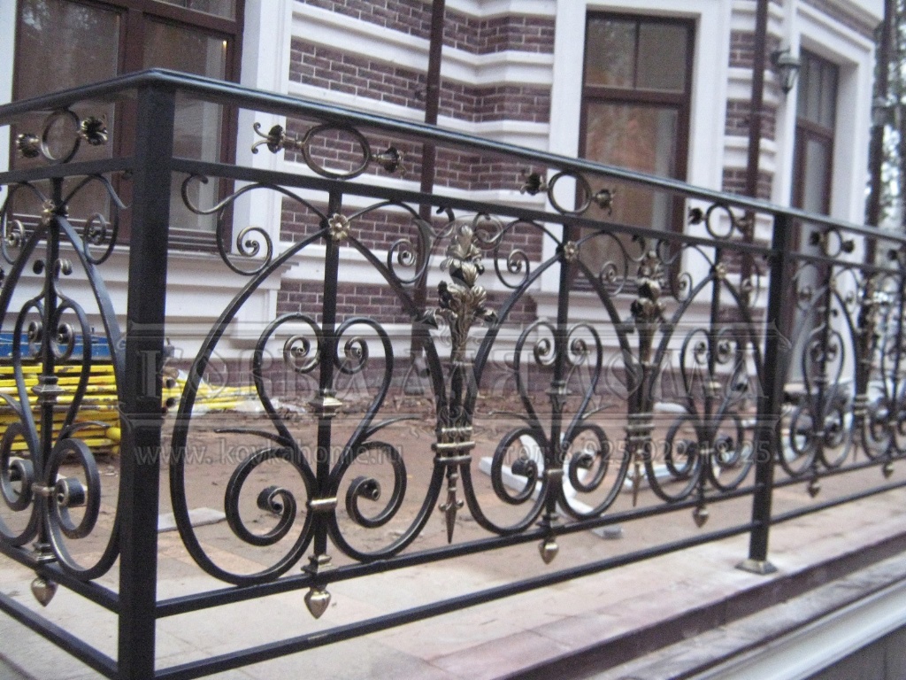 Кованые перила для балкона и крыльца с декоративными балясинами и литыми патинироваными элементами и металлическим поручнем.