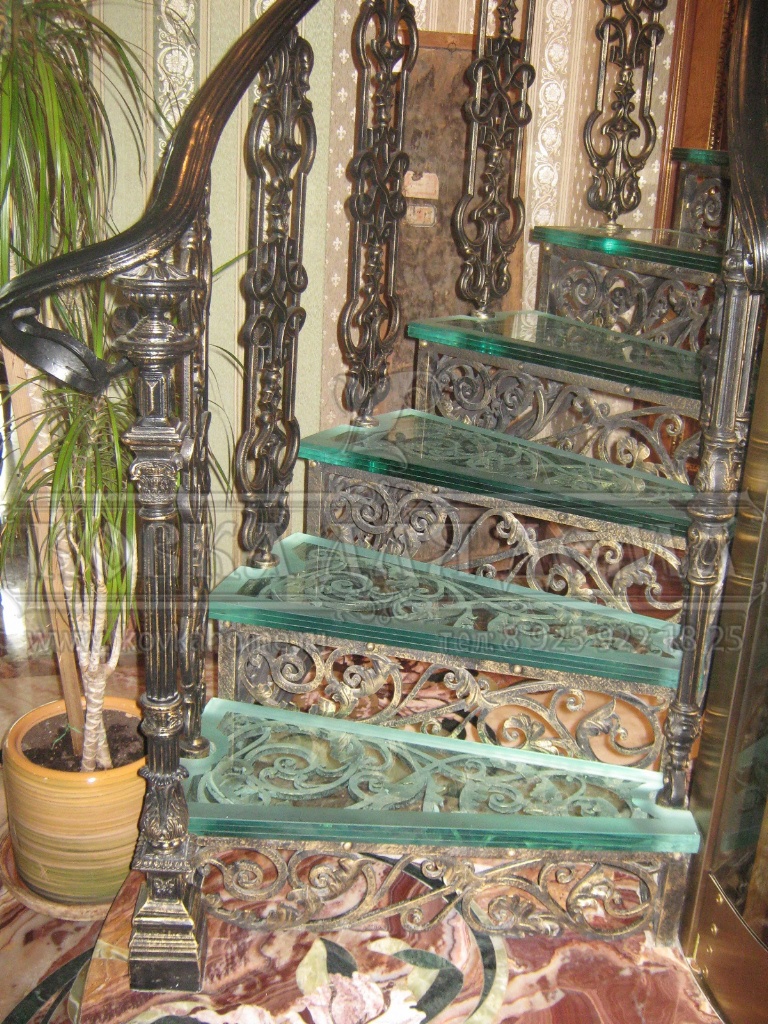 Винтовая каркасная металлическая кованая лестница с кованым декором, стеклянными ступенями и литыми балясинами. 